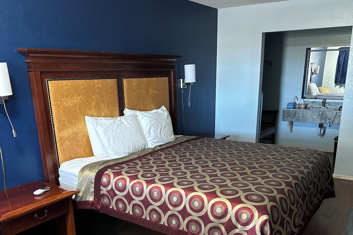 A hotel room with a wooden bed, a nightstand, a chair, and a bathroom visible through an open door.