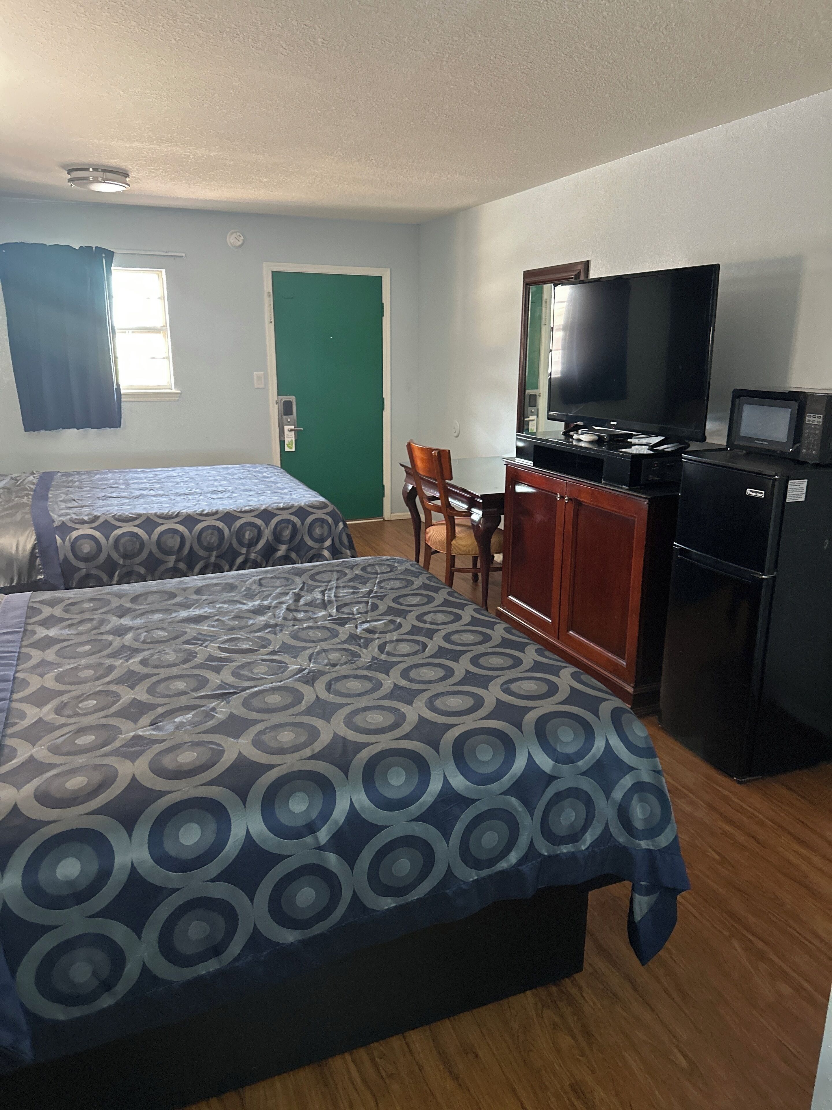 A hotel room with two beds, a TV, a refrigerator, and a small kitchenette.