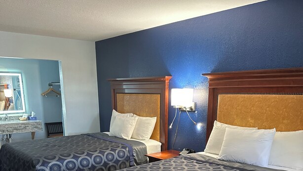 A hotel room with two beds, wooden headboards, a nightstand with a lamp, a mirror, and a wooden chair. - Tanglewood Motel (Frederick)