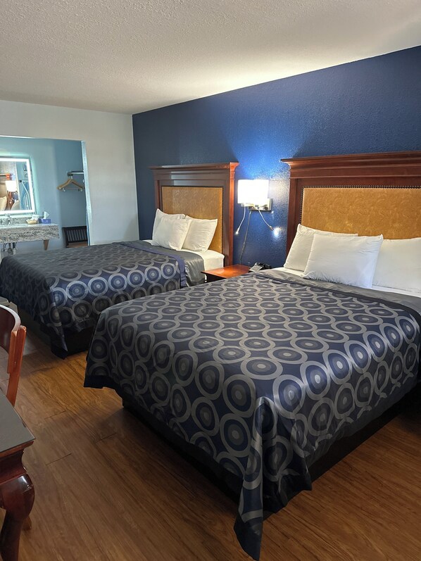 Une chambre d’hôtel avec deux lits, des têtes de lit en bois, une table de chevet avec une lampe, un miroir et une chaise en bois.