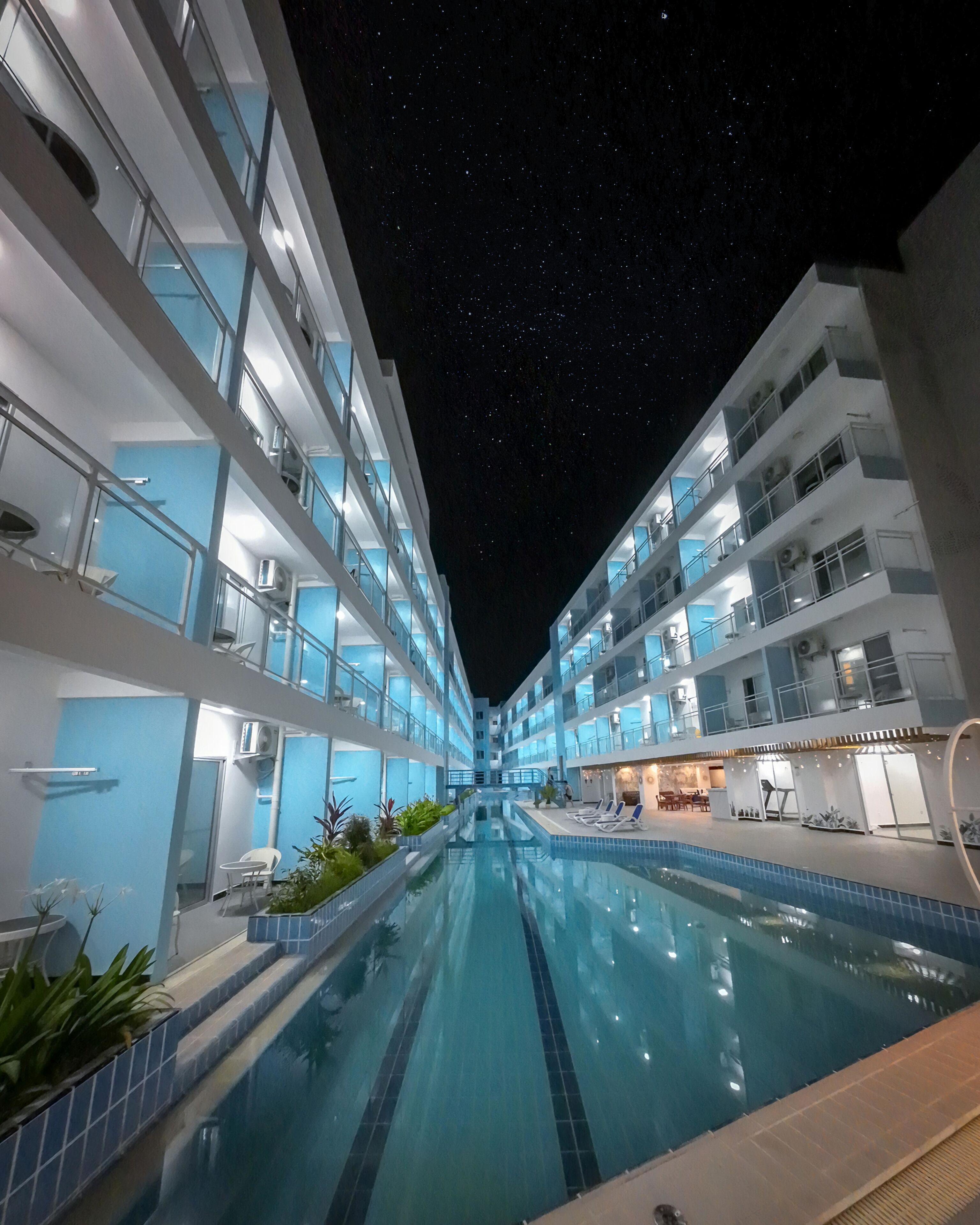 Un hotel con piscina central, varios balcones y un cielo estrellado.