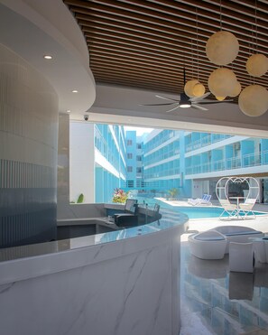 En moderne lobby med reception, et poolområde med liggestole og udsigt til en høj bygning.