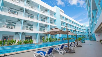 Un hotel de varios pisos con zona de piscina, mobiliario exterior y una escalera que conduce a los pisos superiores.
