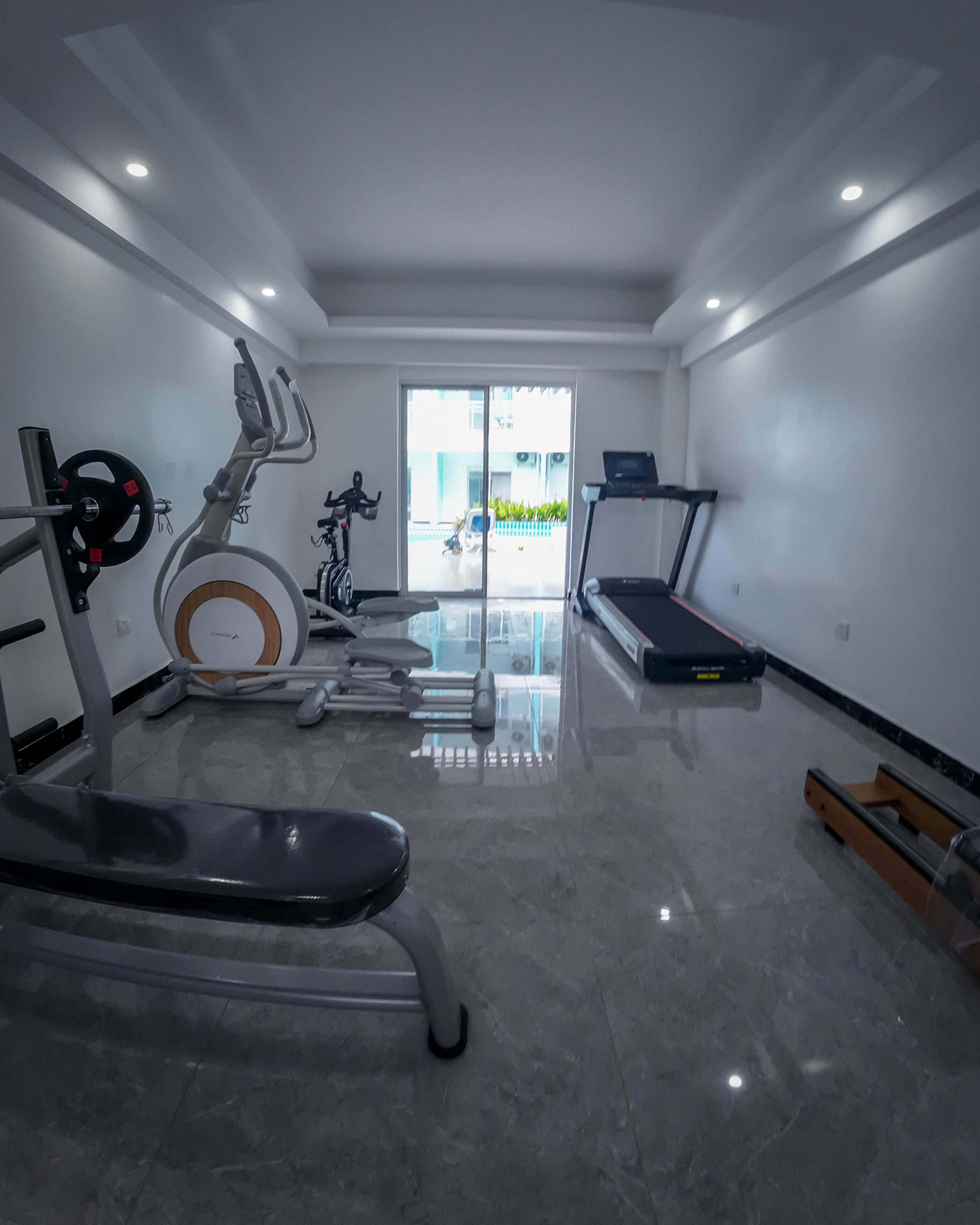 A modern gym with a variety of equipment including a stationary bike, elliptical, treadmill, and weight bench.