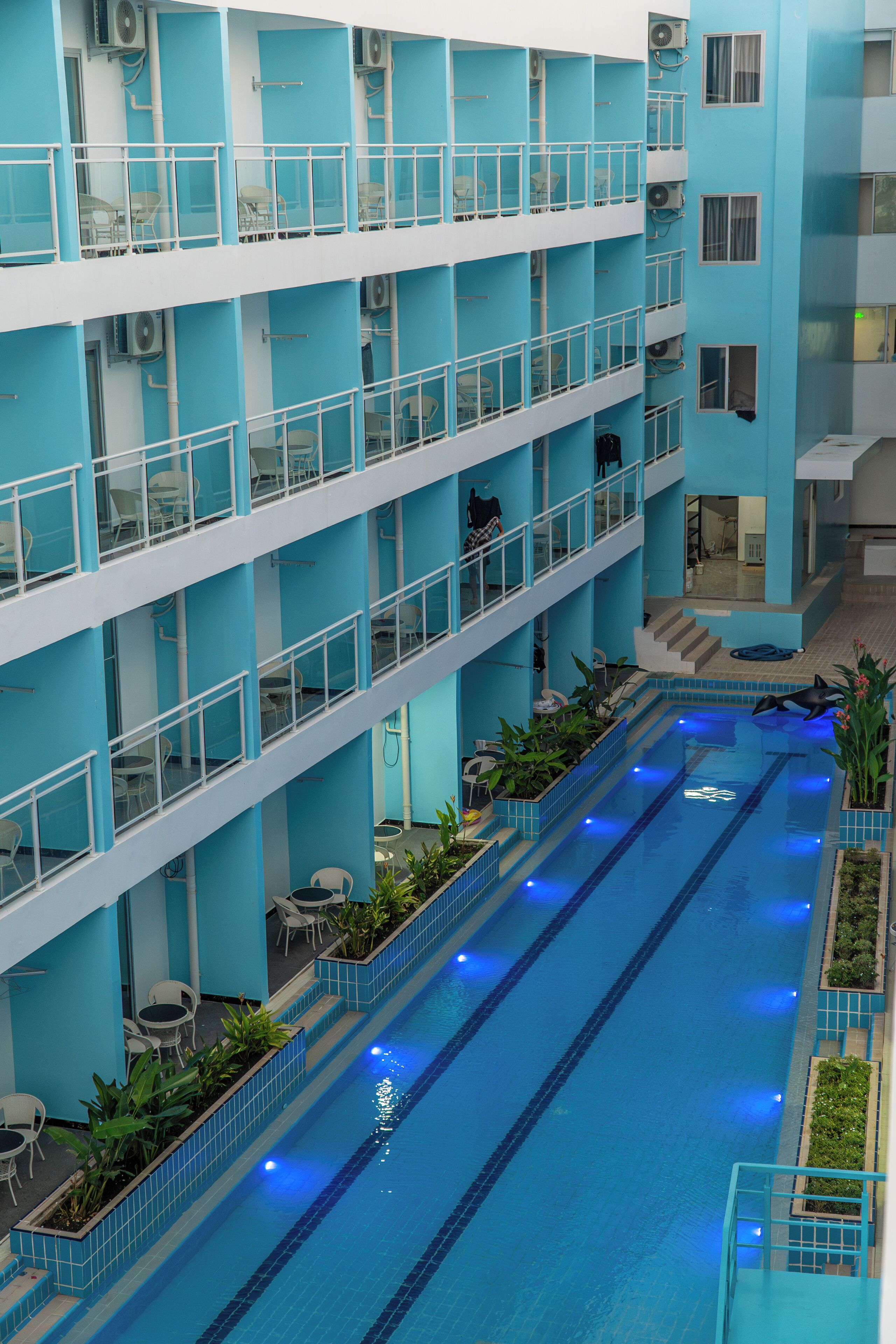 Un hôtel à plusieurs étages doté d’une piscine centrale, de balcons aménagés avec des sièges et de plantes d’intérieur.