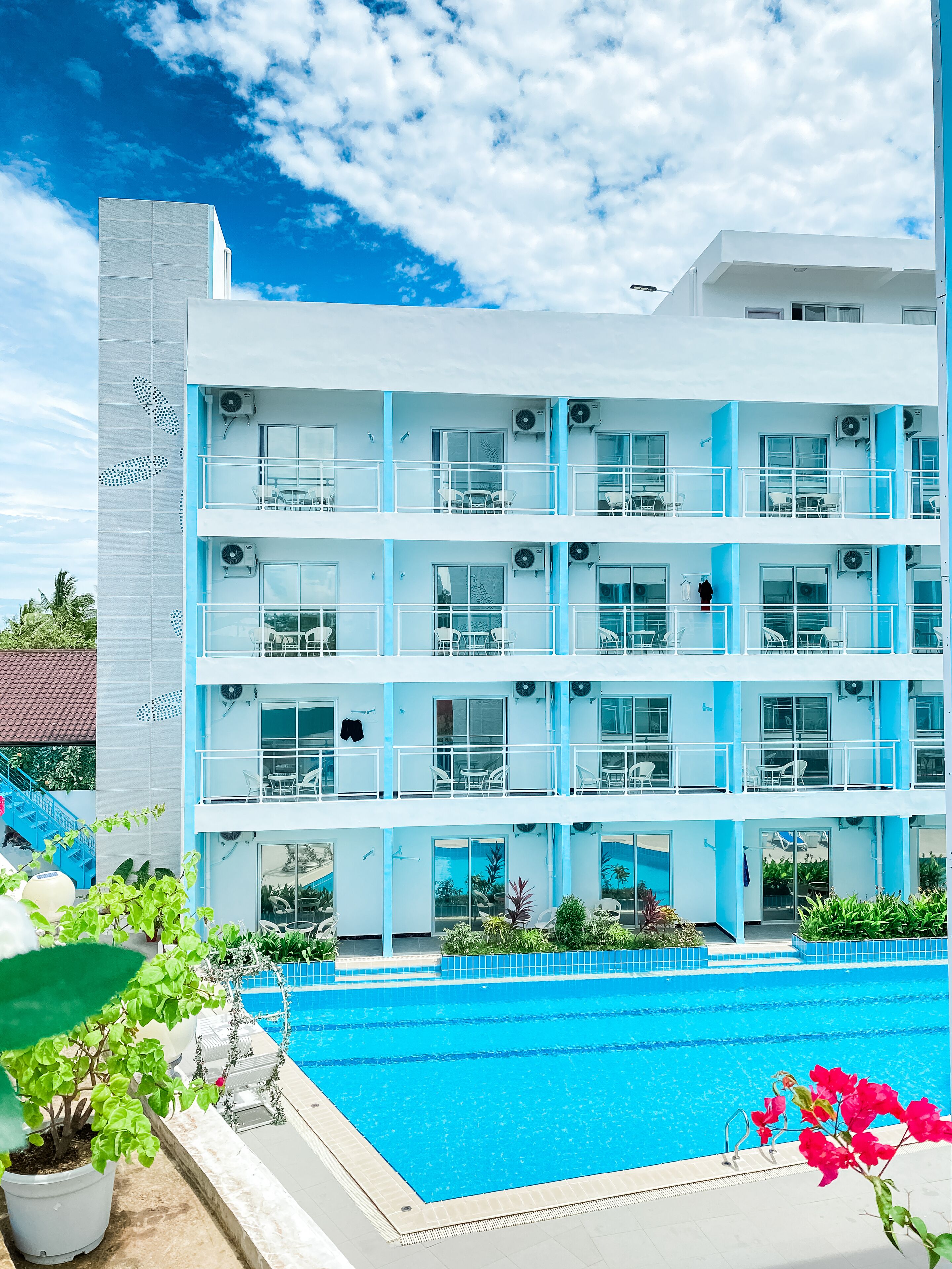 Un hotel de varios pisos con balcones, unidades de aire acondicionado y una piscina.