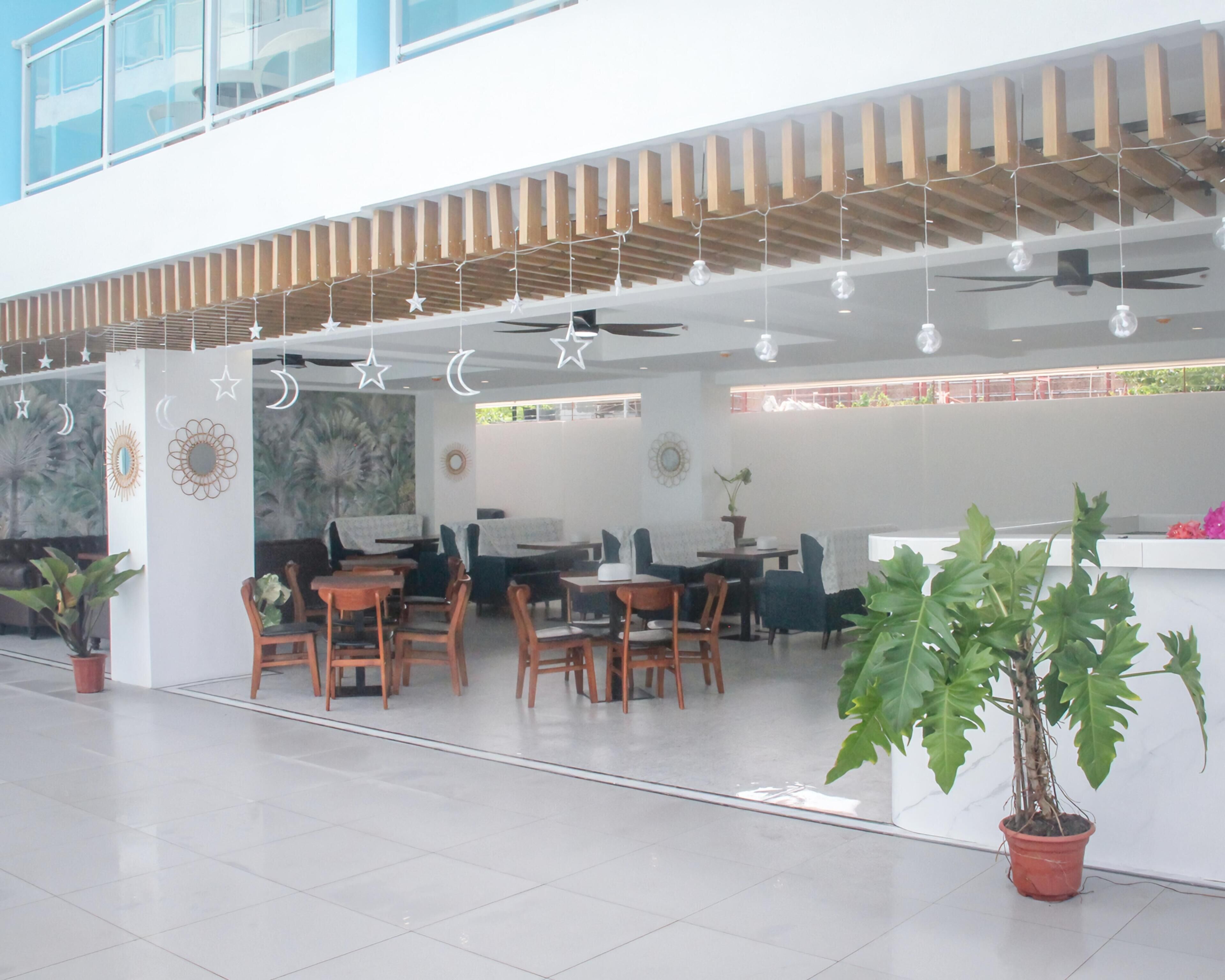 A modern indoor space with wooden ceiling beams, tables, chairs, and potted plants.
