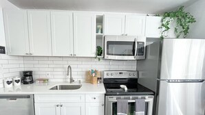 Uma cozinha moderna com armários brancos, geladeira de aço inoxidável, micro-ondas, forno e lava-louças.