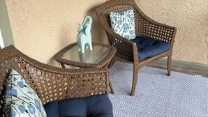 A wicker sofa set with blue cushions and a glass-top coffee table, positioned on a patterned floor. - Siren’s Call, with only a 4 min walk to the beach, is truly irresistible!  (Panama City Beach)
