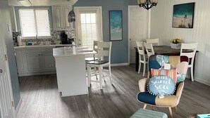 A spacious living area with a dining table and chairs, a kitchen with white cabinets, and a ceiling fan. - Siren’s Call, with only a 4 min walk to the beach, is truly irresistible!  (Panama City Beach)