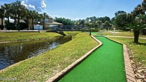A pathway with artificial grass, a small water channel, and a bridge. - Siren’s Call, with only a 4 min walk to the beach, is truly irresistible!  (Panama City Beach)