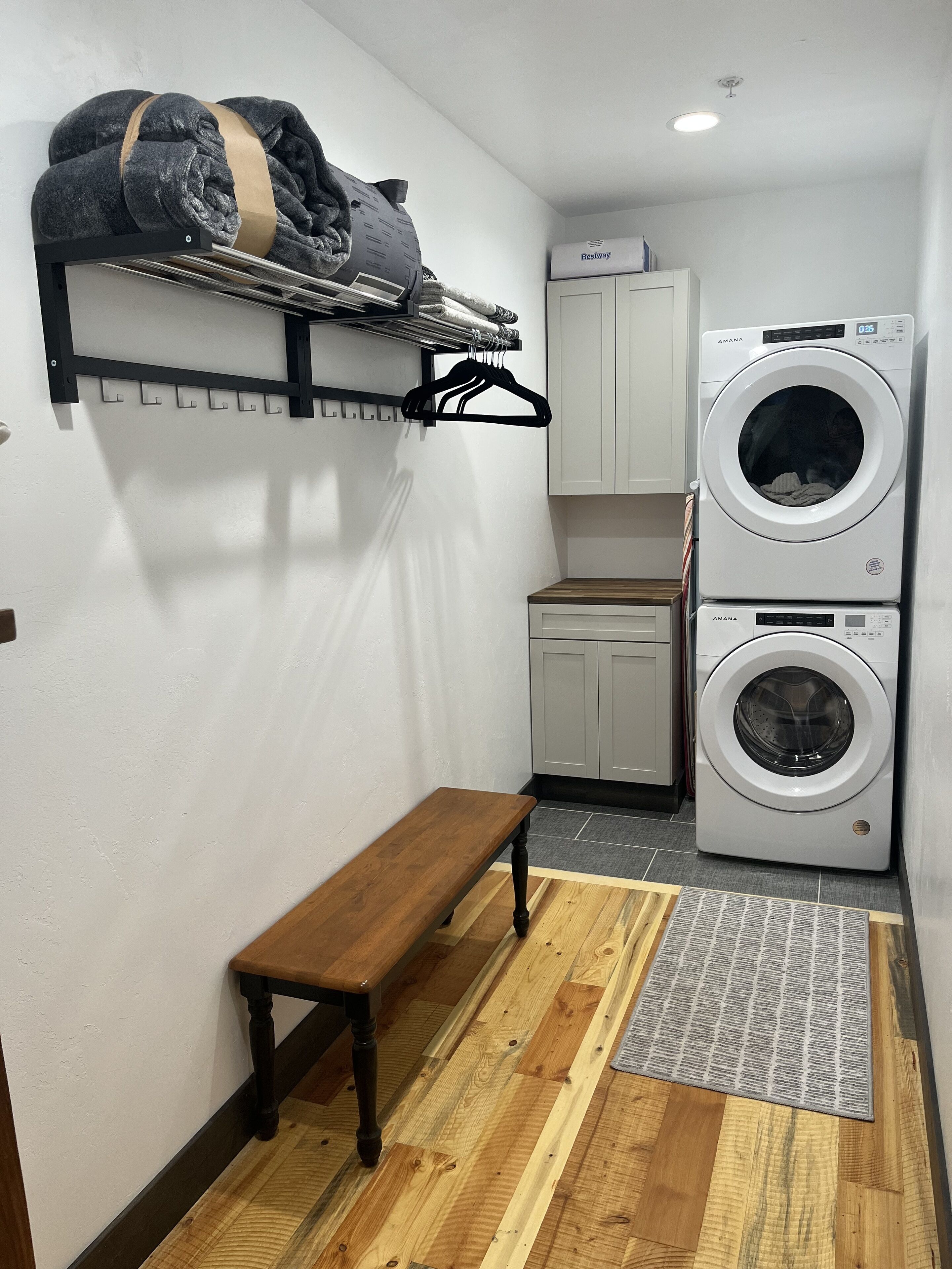 A laundry room with a washing machine, a drying rack, a bench, and a cabinet.