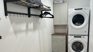A laundry room with a washing machine, a drying rack, a bench, and a cabinet.