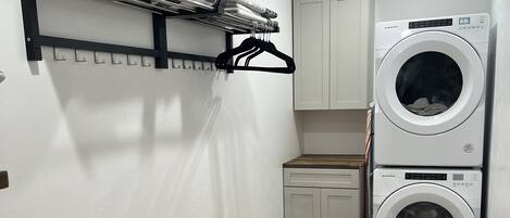 A laundry room with a washing machine, a drying rack, a bench, and a cabinet.