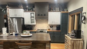 A modern kitchen with a central island, wooden bar stools, a stainless steel refrigerator, a microwave, a stove, and a coffee maker.