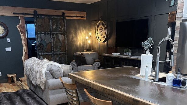 A modern kitchen with a bar area, wooden flooring, and a large clock on the wall.