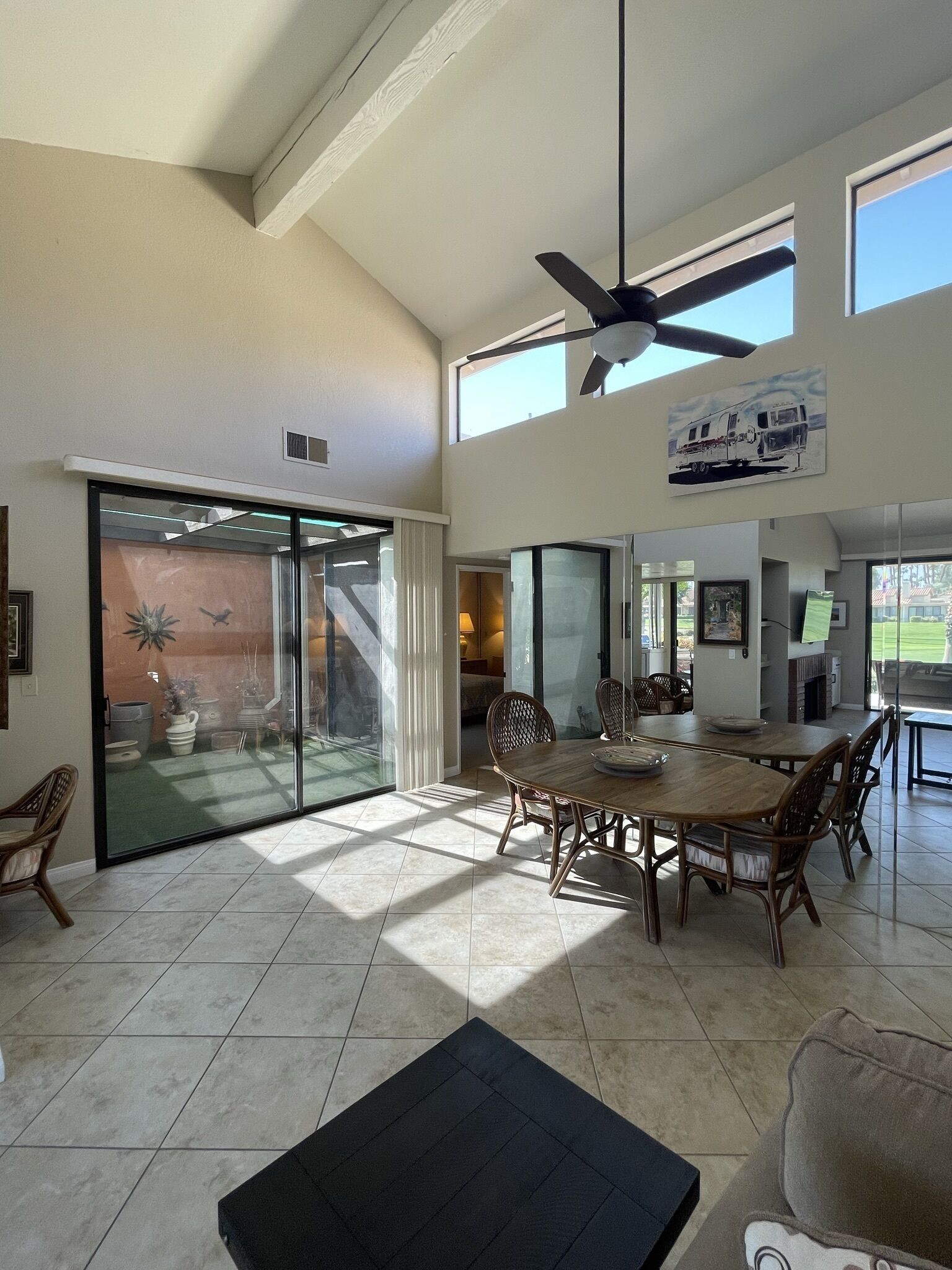 A spacious living area with a large sliding glass door leading to a patio, a dining table with chairs, and a ceiling fan.