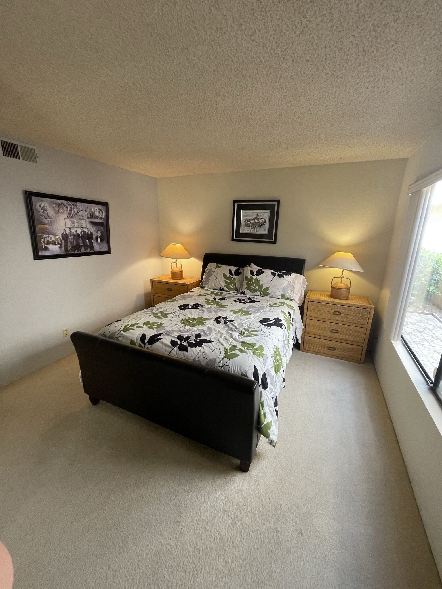 A bedroom with a bed, two nightstands, two lamps, a window, and two framed pictures on the walls.