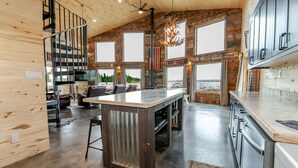 Ein geräumiges Blockhaus-Interieur mit einer zentralen Kochinsel, einer Wendeltreppe und großen Fenstern, die Ausblicke ins Freie ermöglichen.