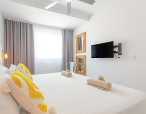 A hotel room with a bed, a flat-screen TV, a window with curtains, and a wall-mounted mirror.