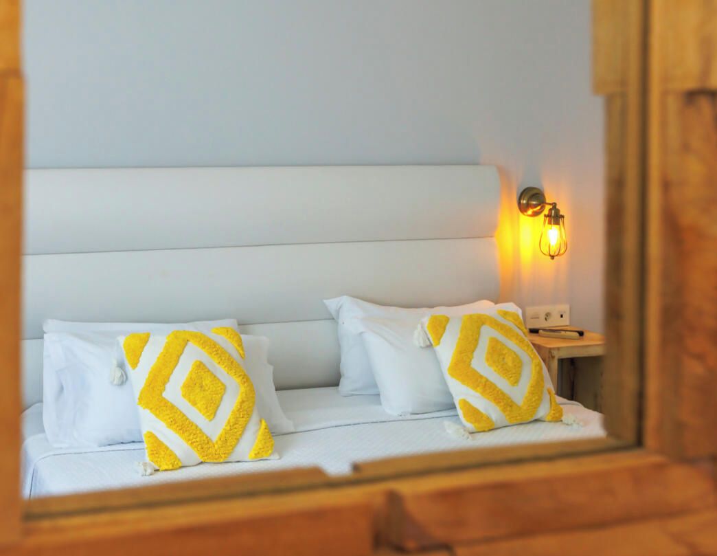 A bed with white bedding and two pillows with a geometric pattern.