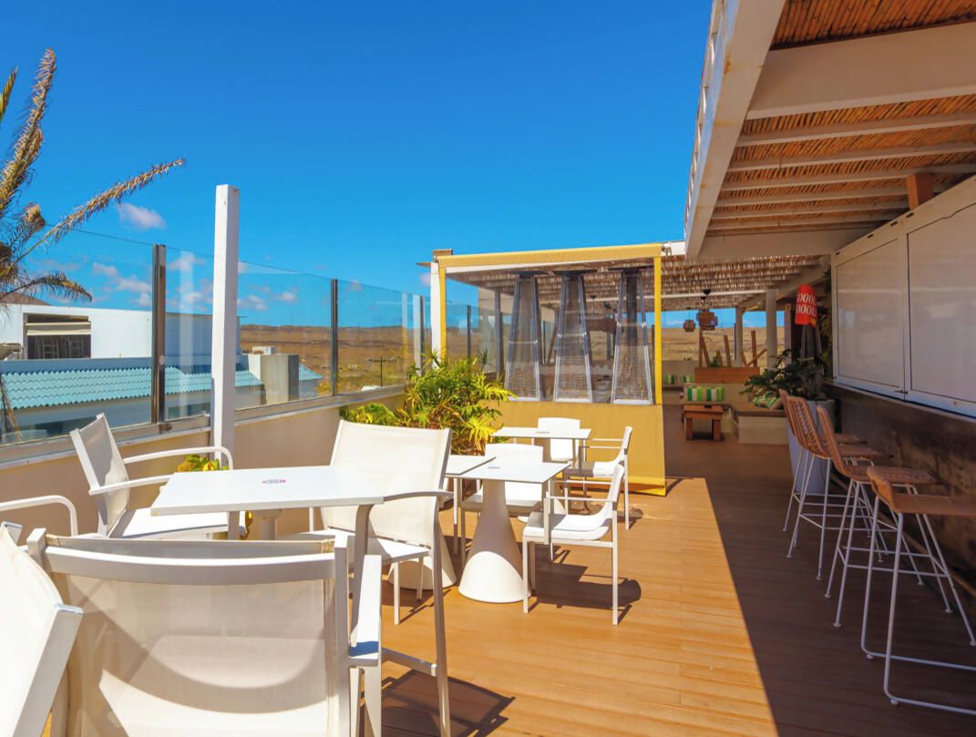Une terrasse extérieure baignée de soleil, avec des tables et des chaises blanches, une plateforme en bois et une vue sur le paysage.