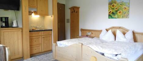 A bedroom with a wooden bed, a wooden wardrobe, and a kitchen area with wooden cabinets and a sink.