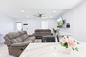 Una sala de estar moderna con un sofá modular, un sillón reclinable, una mesa de centro, un televisor en la pared y una planta.