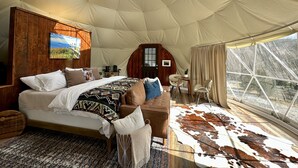 Una habitació amb estructura de tenda espaiosa, amb un llit gran, revestiment de fusta, zona de dinar i vista a l'exterior.