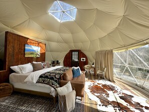 Un'ampia tenda trasformata in stanza, con un letto grande, rivestimenti in legno, un'area pranzo e vista sull'esterno.