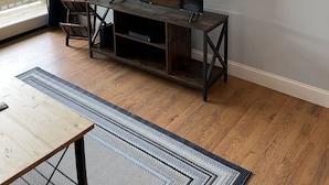 A living room with a TV on a wooden stand, a dining table, and a patterned rug. - Updated condo, Walk to Beech Mountain Resort, Beautiful sunrise, Pet friendly (Beech Mountain)