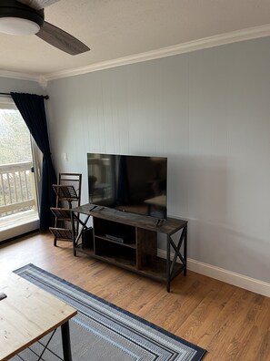 A living room with a TV on a wooden stand, a dining table, and a patterned rug.