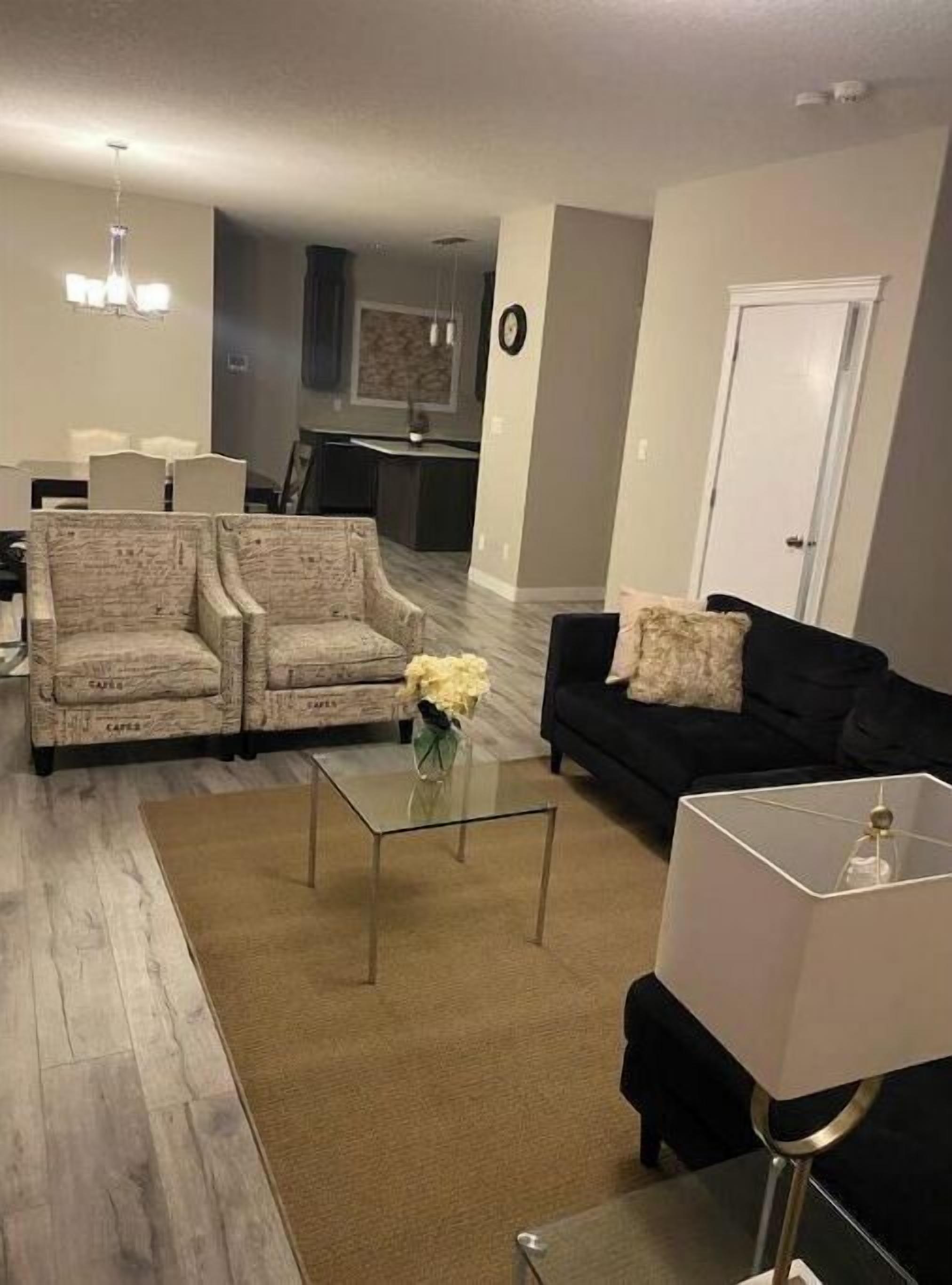 A living room with two armchairs, a black sofa, a glass coffee table, and a lamp.