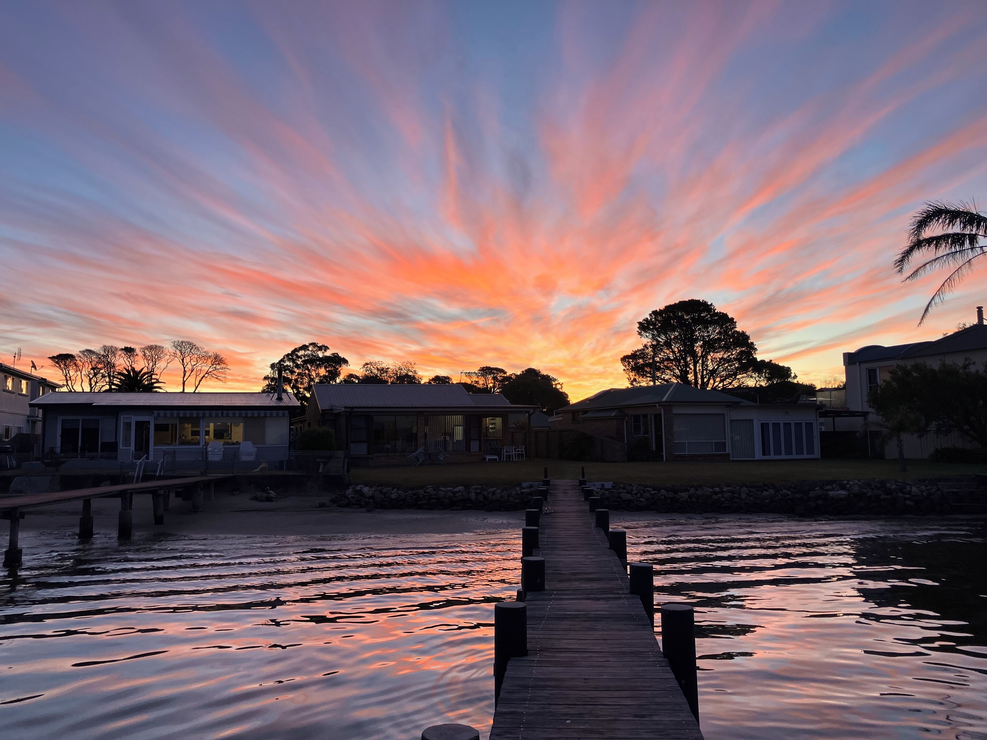 A wooden pier leading to a row of houses with a sunset in the background.