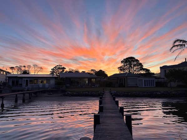 A wooden pier leading to a row of houses with a sunset in the background.