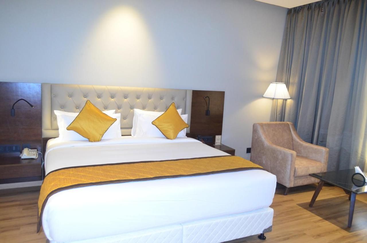 Habitación de hotel con una cama grande, dos almohadas, una mesita de noche, una silla y una lámpara.