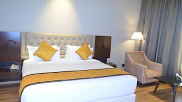Habitación de hotel con una cama grande, dos almohadas, una mesita de noche, una silla y una lámpara.