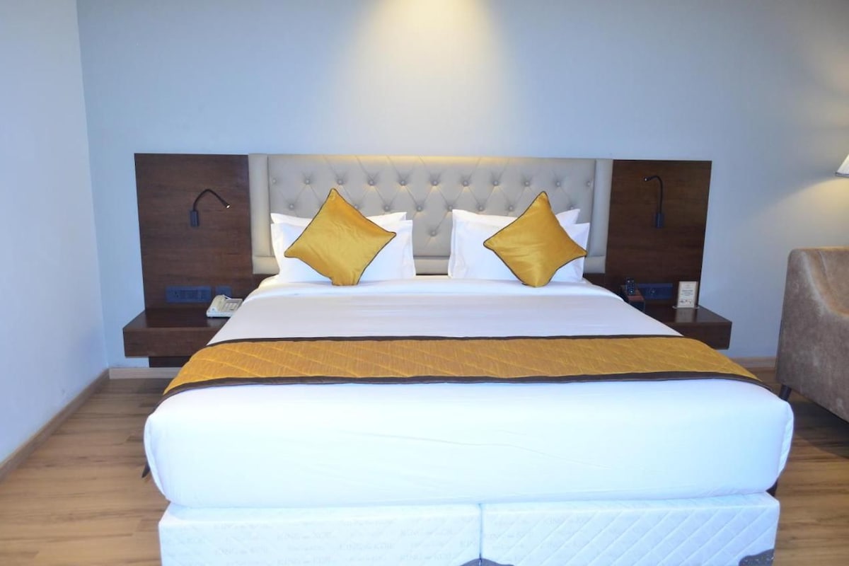 Una habitación de hotel con una cama grande, dos mesitas de noche, un cabecero de madera y un sillón marrón.
