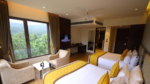 Habitación de hotel con dos camas, un sofá, un televisor y un balcón con vistas a zonas verdes.