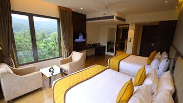 A hotel room with two beds, a sofa, a TV, and a balcony with a view of greenery.