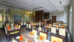Comedor con varias mesas dispuestas para los huéspedes, área de cocina y mostrador de recepción.