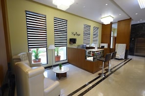 Vestíbulo de hotel con mostrador de recepción, zona de estar y amplias ventanas con persianas.