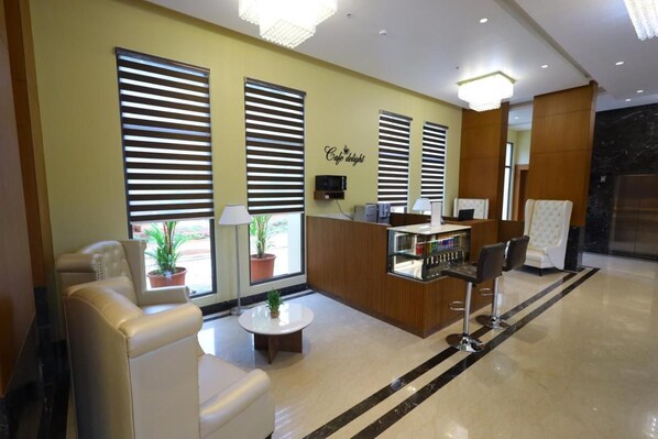 A hotel lobby with a reception desk, seating area, and large windows with blinds. - The Aurum Subrahmanya (Sullia)