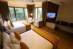 Habitación de hotel con dos camas, un escritorio, una silla, un televisor y ventanas amplias con cortinas.