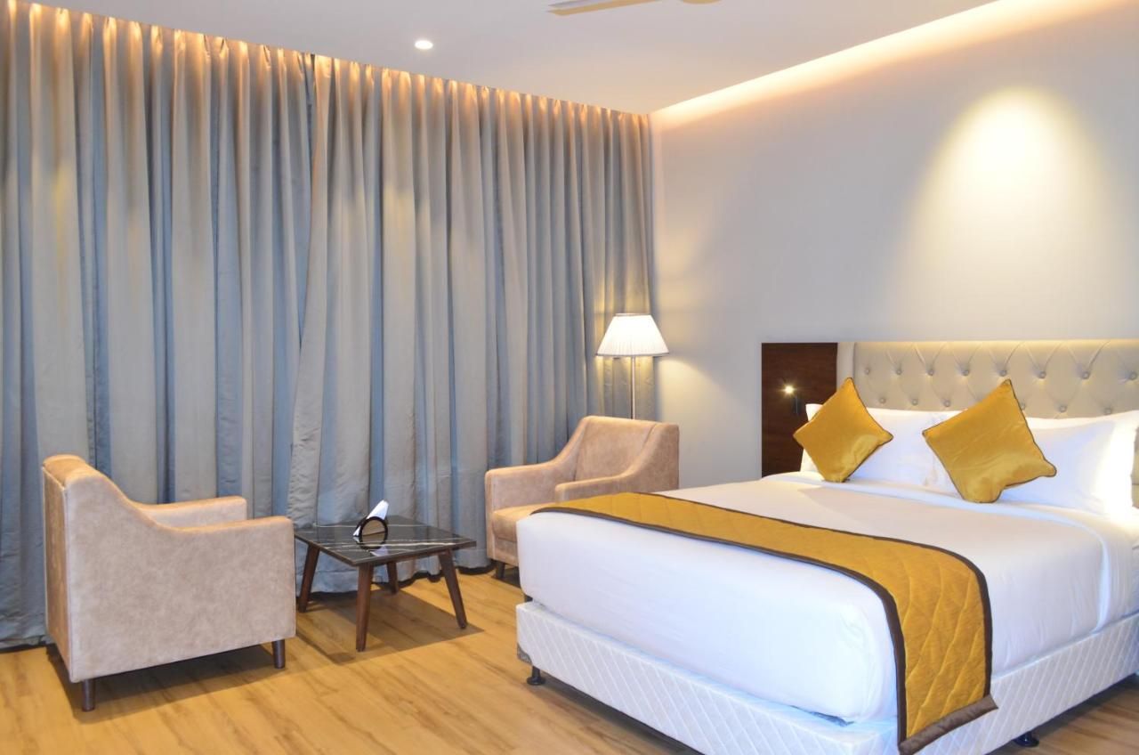 A hotel room with a large bed, two armchairs, a small table, and a lamp.