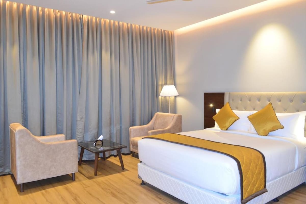 Una habitación de hotel con una cama grande, dos sillones, una mesita y una lámpara.