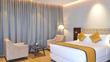 A hotel room with a large bed, two armchairs, a small table, and a lamp.
