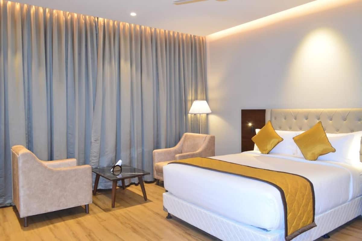 A hotel room with a large bed, two armchairs, a small table, and a lamp.