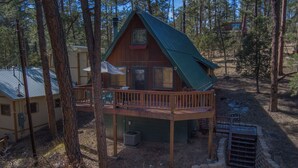 A cabin with a wooden deck, a covered porch, and a metal roof, surrounded by trees. - Cozy Upper Canyon Gem w Large deck and Great Forest Views (Ruidoso)