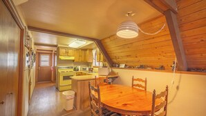 A cozy kitchen with wooden cabinets, a stove, and a dining area with a wooden table and chairs. - Cozy Upper Canyon Gem w Large deck and Great Forest Views (Ruidoso)